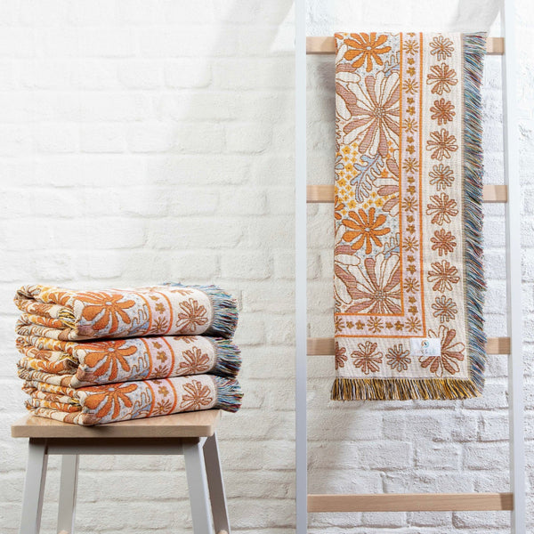 Stack of floral patterned blankets on a stool against a white brick wall.