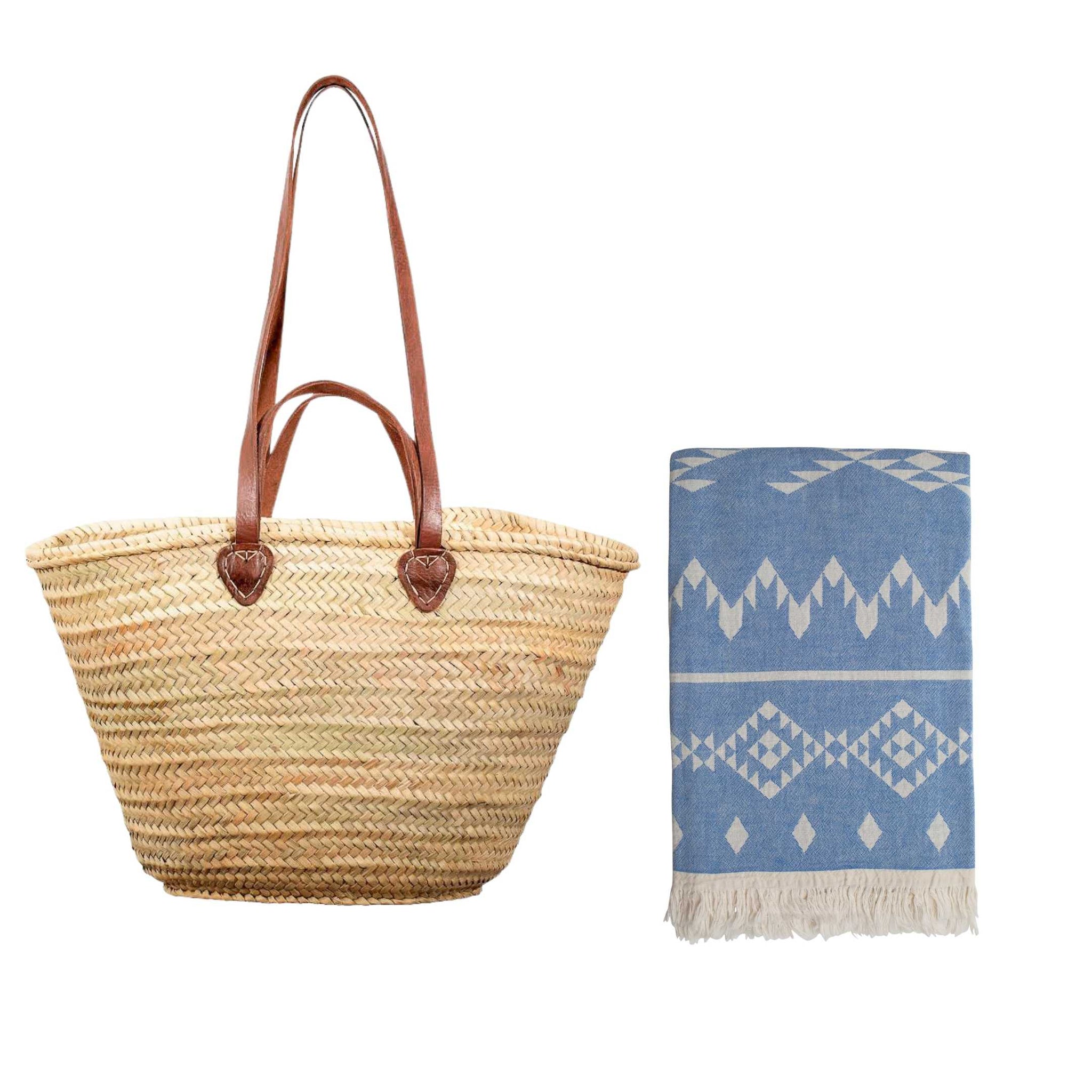 Woven straw bag with brown handles and a blue and white patterned hammam towel on a white background