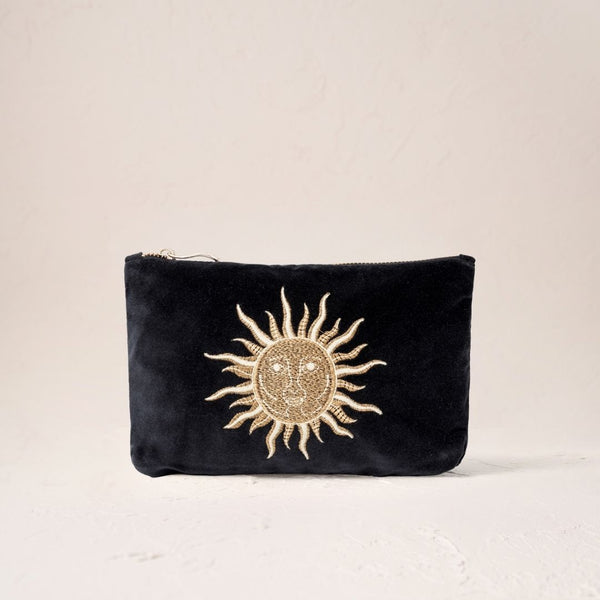 Elizabeth Scarlett black velvet mini pouch with gold embroidered sun design on a beige background.