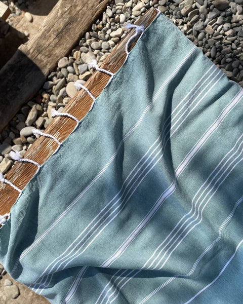 Green striped hammam towel with white stripes on a wooden surface with pebbles in the background