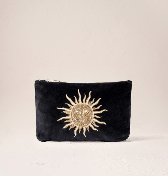 Elizabeth Scarlett Black velvet mini pouch with embroidered gold sun design on a beige background.