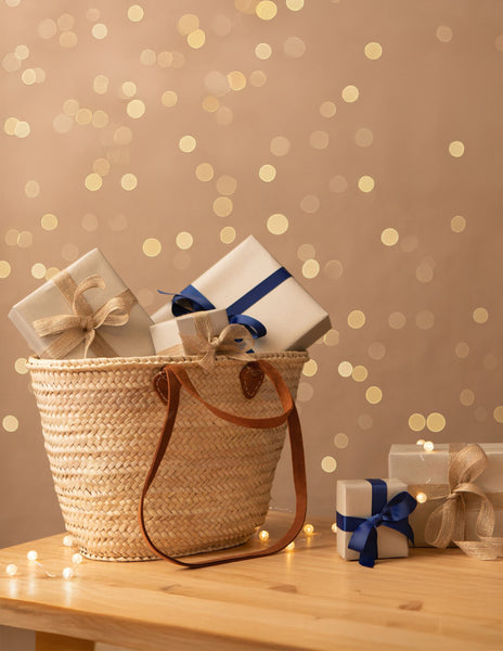 Straw basket bag with chestnut brown leather handles, filled with wrapped presents.