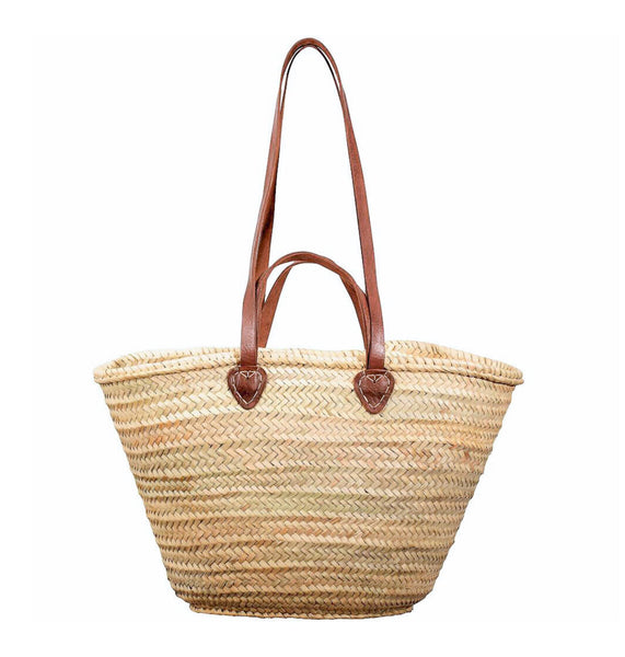 Woven straw basket bag with brown leather handles on a white background