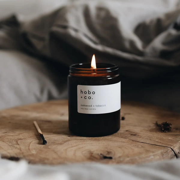 Lit Hobo & Co jar candle on a wooden surface with a blurred background