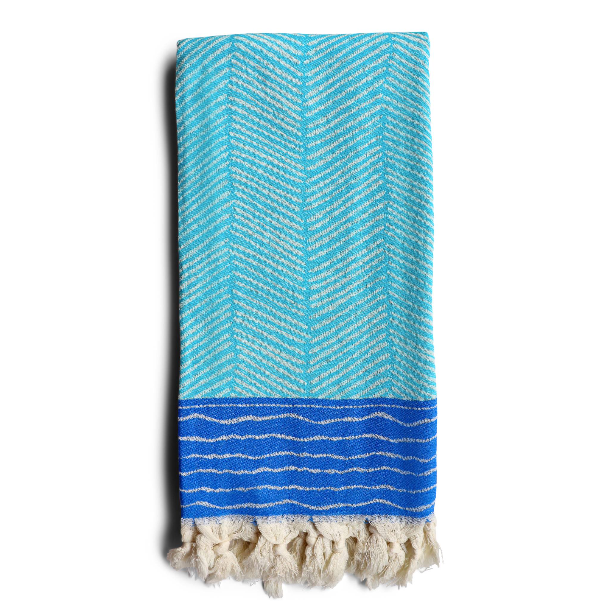 image of folded Skiathos hammam towel with a turquoise and cobalt blue design on an off-white background. Fringing at both ends. Sold by Sand and Salt.