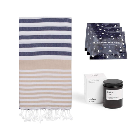 Winter retreat gift bundle containing striped hammam towel, three 'spacemasks' and a 'hobo & co.' jar candle on a white background.