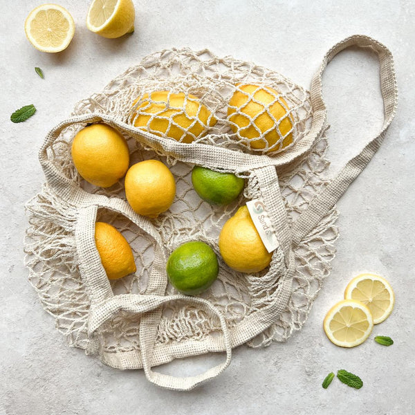 Image of a reusable organic cotton string shopping bag, natural coloured with lemons and limes inside.